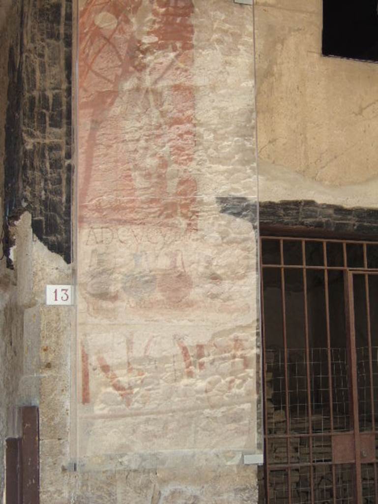 VI.13 Herculaneum on left, VI.14 on right. May 2006.
Painted sign on pilaster between house entrance and shop. Looking south.
At the top is a painted figure.
The shop sign showed four jugs of different colours, naming and pricing the drinks sold here together with the shop sign AD CVCVMAS (Ad Cucumas), written above the jugs.
The painted graffiti NOLA in red letters can also be seen on the lower part.